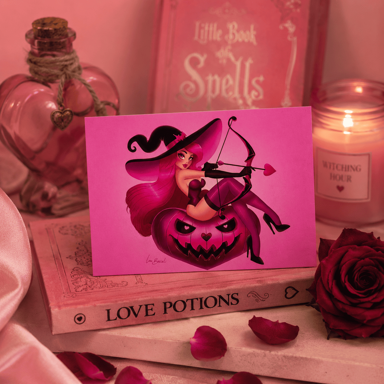 Carte postale Love Witch représentant une pin-up sorcière assise sur une citrouille, présentée dans une ambiance romantique.